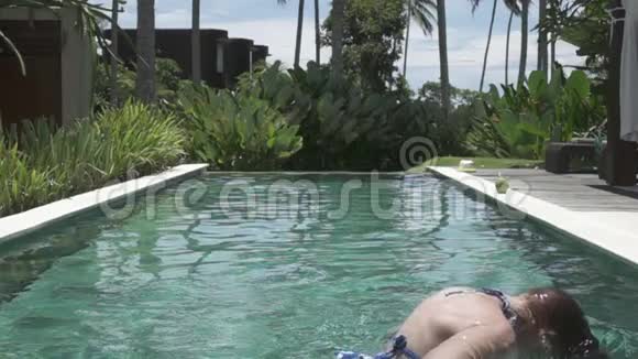 动作缓慢游泳池边的年轻苗条的女人在热带度假胜地扔出湿漉漉的长发视频的预览图