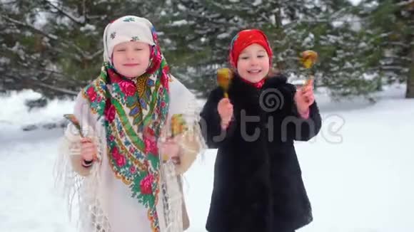 两个穿着俄罗斯风格的衣服和头巾的小女孩在雪地里用木勺玩视频的预览图