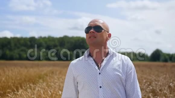 一个穿着白色衬衫的秃头站在金色麦田里的肖像在阳光明媚的天空背景上歌唱视频的预览图
