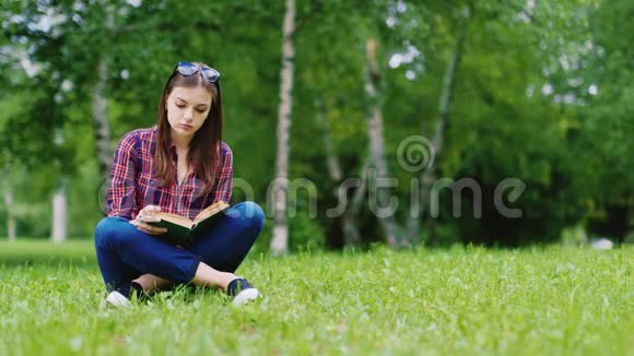 迷人的女学生在公园里看书坐在草坪上视频的预览图