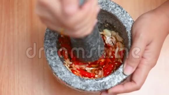 女式手用灰泥打红热鲜辣椒蒜末烹饪前准备拌料视频的预览图