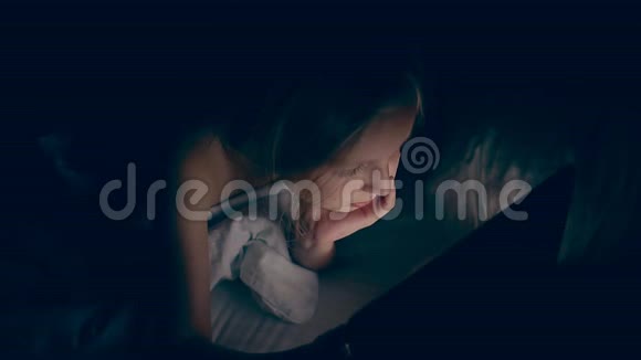 年轻的白种人女孩晚上躺在床上玩平板电脑上网低键手持视频的预览图