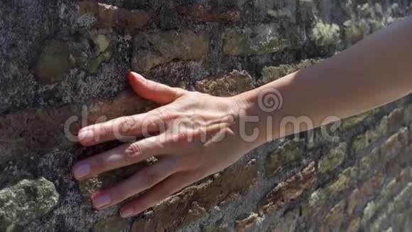 女人用手慢慢地靠在旧红砖墙上女性手触摸粗糙的石头表面视频的预览图