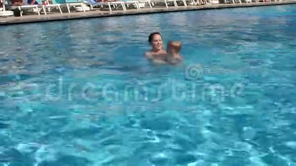 一个年轻的女人教一个孩子在游泳池里的水里游泳慢动作视频的预览图