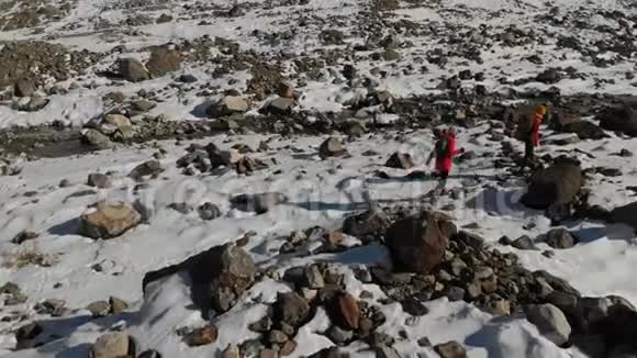 两位带着背包和照相机的女旅行者的空中景色穿过雪地和石头来到冰川之间视频的预览图