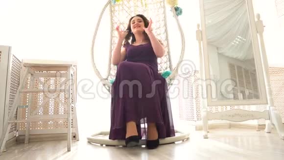 穿紫色衣服的美丽女性坐在豪华内部的圆形藤椅上视频的预览图