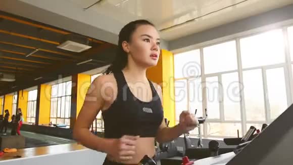 年轻的亚洲女孩在健身房的椭圆教练上做运动视频的预览图