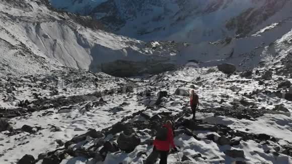 两位带着背包和照相机的女旅行者的空中景色穿过雪地和石头来到冰川之间视频的预览图