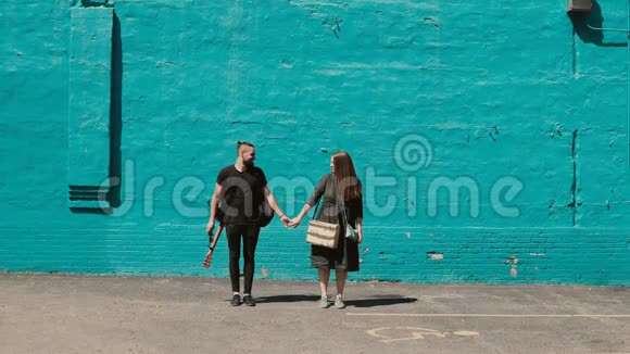 年轻漂亮的夫妇在明亮的蓝色墙壁附近摆姿势英俊的男人拿着吉他女人拿着素描盒视频的预览图