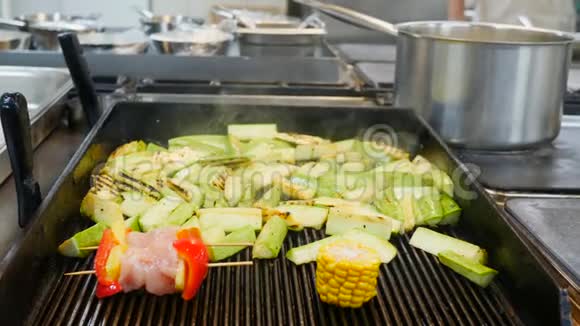 在一家模糊的餐厅厨房背景下烤架上炸着发烟的蔬菜胡椒西葫芦肉片玉米片视频的预览图