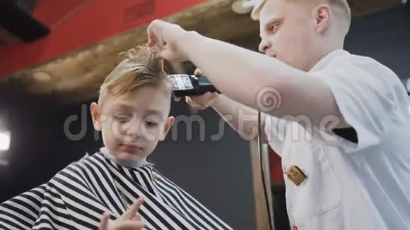 一个专业的理发师为理发店里一个漂亮的小男孩做一个时尚的发型漂亮的男孩是视频的预览图