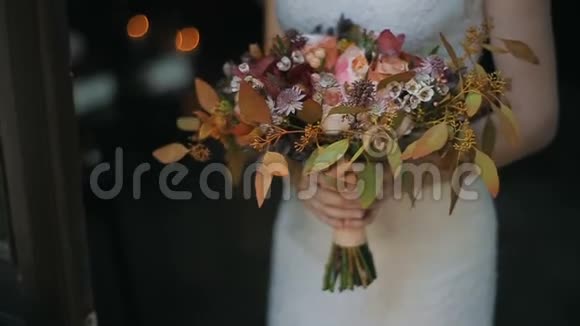 新娘手中的婚礼花束在室内在背景上点燃蜡烛新娘手里捧着漂亮的婚礼花束视频的预览图