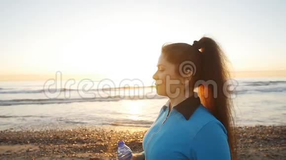 年轻的运动女性在海边日落时在室外饮水视频的预览图