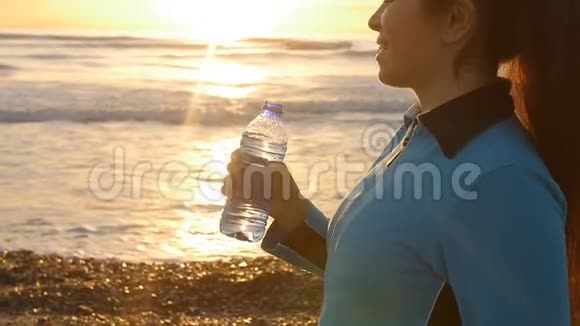 年轻的运动女性在海边日落时在室外饮水视频的预览图