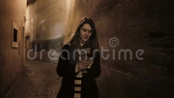 年轻时尚的女人深夜穿过废弃的小巷街道用智能手机聊天视频的预览图