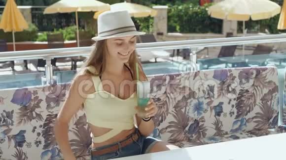快乐女孩在阳光明媚的海滩上喝鸡尾酒对着镜头微笑视频的预览图