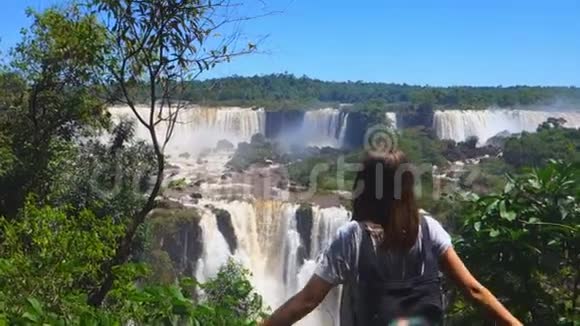 那个女孩站在一个大瀑布的背景上伸出双臂站立视频的预览图