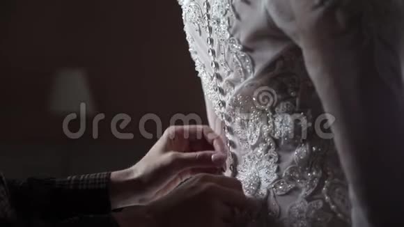 钮扣新娘婚纱特写双手在室内的婚纱上系扣子视频的预览图
