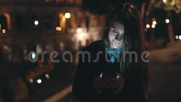 慢动作年轻的黑发女人晚上在意大利罗马竞技场附近散步使用智能手机视频的预览图