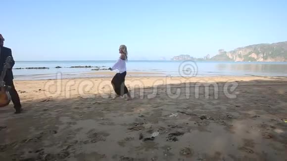 女孩在海滩上追上胡子吉他手他带着她转身视频的预览图