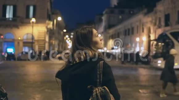 背着背包的年轻旅游妇女站在交通道路上晚上四处张望视频的预览图