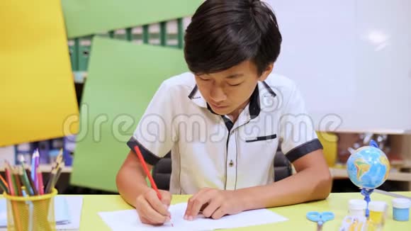 男孩坐在桌子旁用红色铅笔在笔记本上写字视频的预览图