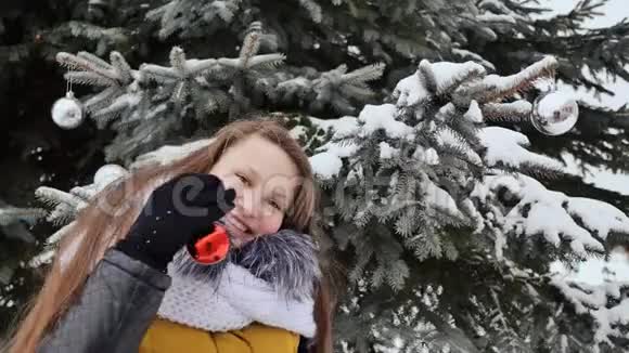 迷人的年轻女孩留着长发穿着冬装对着一棵雪树摆姿势一个女孩在串圣诞球视频的预览图