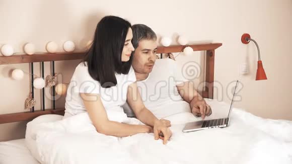 幸福夫妻在家里床上用笔记本电脑上网购物视频的预览图