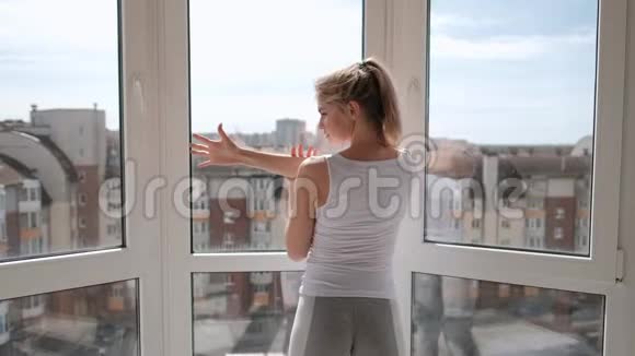 年轻漂亮的运动女性金发穿着白色运动服在家里的阳台上做瑜伽和伸展运动准备就绪视频的预览图
