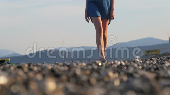 夕阳西下瘦小女子的腿在鹅卵石海岸上行走海浪在冲刷海岸视频的预览图