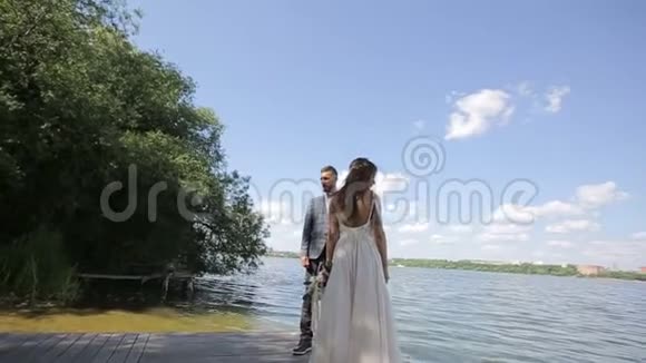 一对年轻漂亮的新婚夫妇站在湖边结婚纪念日慢动作视频的预览图