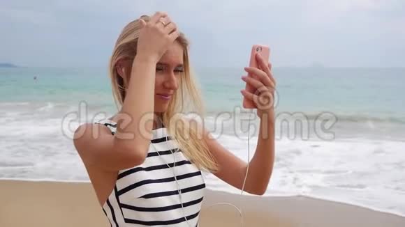 年轻漂亮的苗条女人一头金发穿着黑白连衣裙看着她的手机女孩用电话视频的预览图