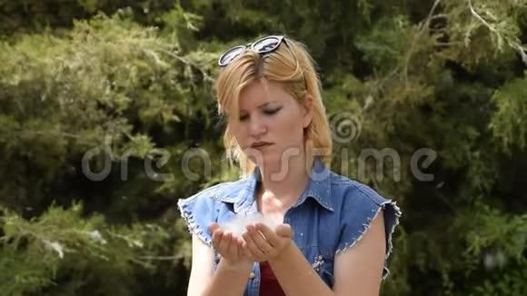 一个金发女人吹着杨树的绒毛一个女孩手里的杨树绒毛视频的预览图