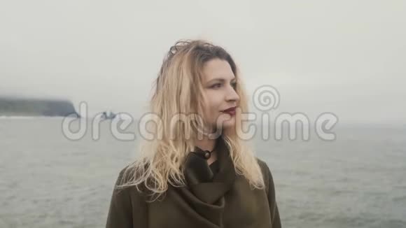 年轻的金发女人站在黑色的海滩上靠近冰岛的巨魔脚趾环顾四周头发随风飘扬视频的预览图