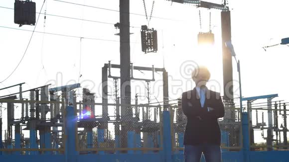 一个戴着白色头盔和黑色眼镜的人站在电站的背景下双臂交叉交叉日落视频的预览图