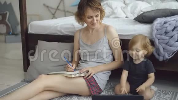 幸福家庭可爱可爱的女儿坐在家里床边用铅笔画相册视频的预览图
