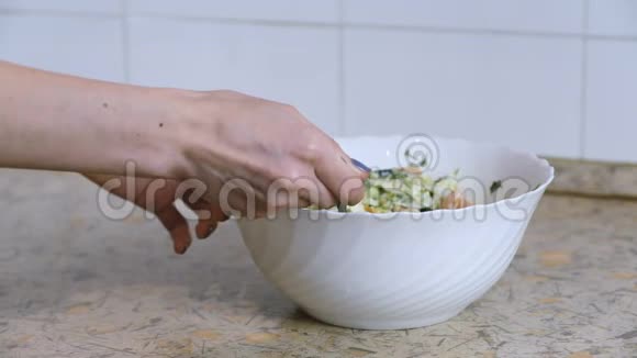在厨房桌子上的一个白色盘子里女人手混合蔬菜沙拉侧视Slomo视频的预览图