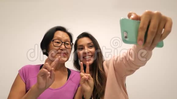 退休母亲和年轻女儿展示和平标志和制作有趣的自拍照片与手机4K视频的预览图