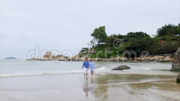 年轻快乐的一对美丽的恋人穿着蓝色的衣服牵着手沿着海滨散步谈笑风生视频的预览图