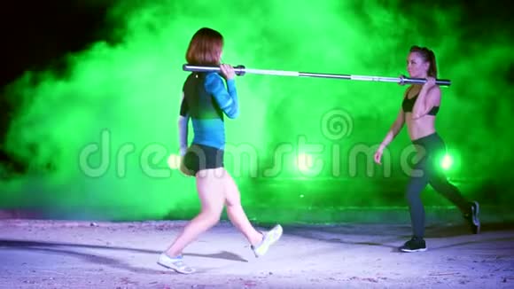 两个运动女孩成双成对地做各种力量练习用杠铃蹲晚上轻烟视频的预览图