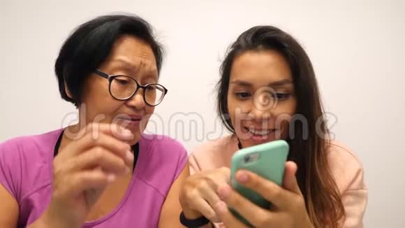 年长混合种族妇女和年轻的微笑女儿在家使用现代小玩意4K视频的预览图