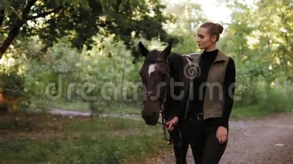 年轻的美女在森林里一起散步时正抚摸着一匹前额有白斑的令人惊叹的棕色马视频的预览图