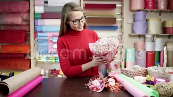 在花店里一个穿红色跳线的快乐花店女人用纸包花她试图用一种视频的预览图