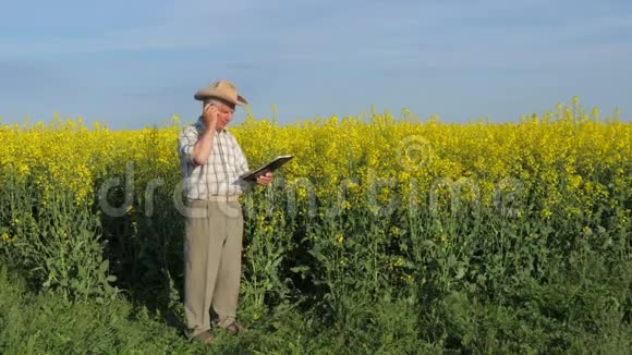 农夫站在郁郁葱葱的黄田里拿着一个文件夹在电话里视频的预览图
