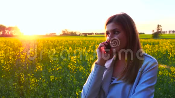 年轻漂亮的女人用智能手机在夕阳田野的剪影上视频的预览图