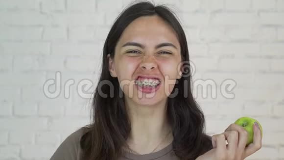 戴着牙套的女人吃着绿苹果微笑着白色的特写视频的预览图