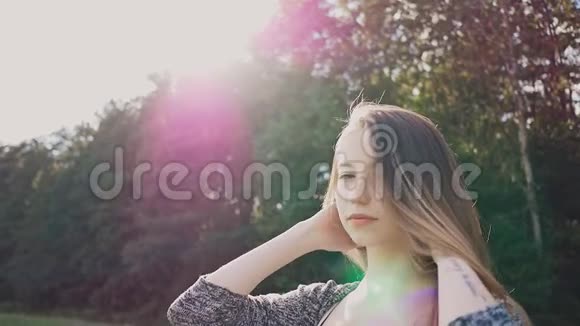 年轻而迷人的女孩在美丽的紫色晚霞中的绿树背景上对着镜头摆姿势视频的预览图