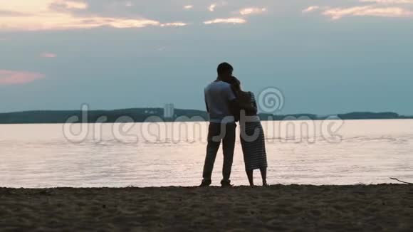 站在河边的年轻幸福夫妇的后景男人和女人在海滩上拥抱日落视频的预览图