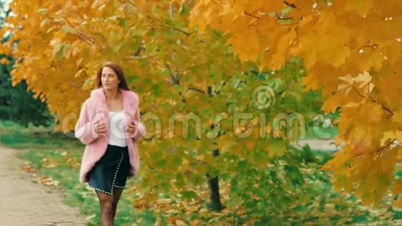 秋天公园里的年轻女子穿着粉红色的衣服走在枫树黄树旁摆着姿势视频的预览图