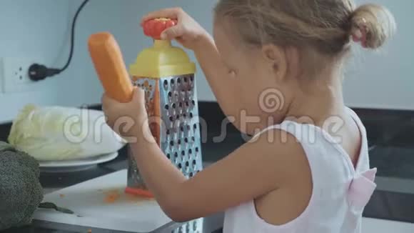 可爱的小女孩在家庭厨房的烤炉上摩擦胡萝卜视频的预览图